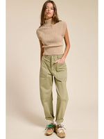 Model wearing a SLEEVLESS KNIT TURTLENECK in camel with green cargo pants.