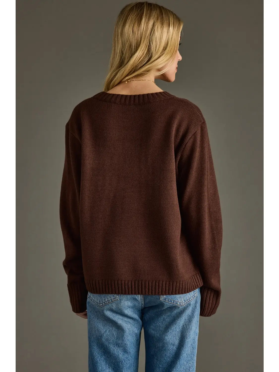 Back view of a woman wearing a dark brown coffee weather sweater with blue jeans.