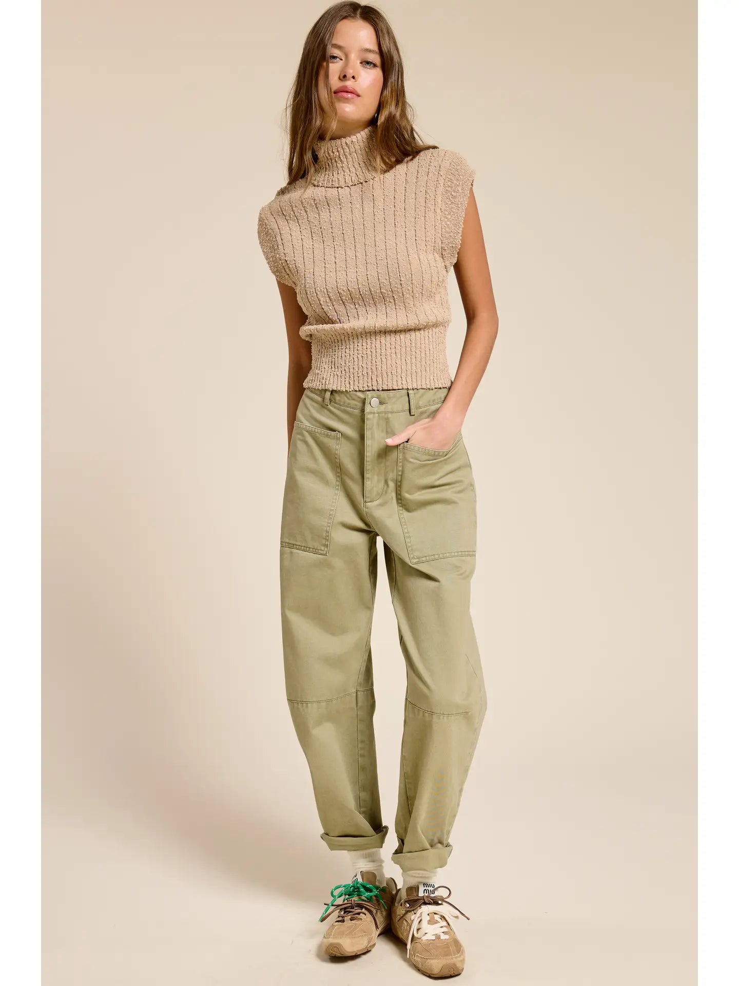 Model wearing a SLEEVLESS KNIT TURTLENECK in camel with green cargo pants.